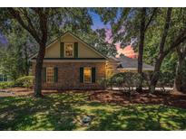 Charming brick home with green shutters nestled among mature trees in a lush, green lawn at 90 Old Carriage Ln., Pawleys Island, SC 29585