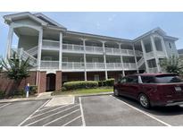 Three story condo building with brick facade and covered outdoor hallways, light green siding, and a maroon Kia van at 1514 Lanterns Rest Dr. # 103, Myrtle Beach, SC 29579