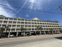 Spacious condo building with multiple floors of units, balconies, street parking, and some palm trees at 200 53Rd Ave. N # 205, North Myrtle Beach, SC 29582