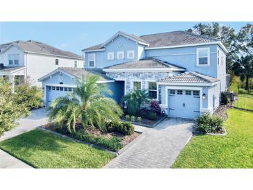 Two-story house with light blue exterior, stone accents, and a three-car garage at 1457 Olympic Club Blvd, Champions Gate, FL 33896