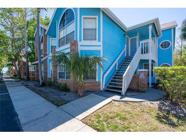 Charming blue condo featuring multiple windows, a small palm tree, and convenient stairwell access to the entrance at 2735 N Poinciana Blvd # 103, Kissimmee, FL 34746