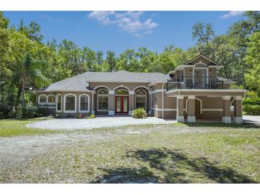 Stunning two-story home with arched windows, red door, balcony, and a circular driveway at 445 Se 98Th Ave, Webster, FL 33597