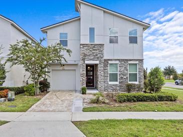 Charming two-story home features a stone facade, manicured lawn, paver driveway, and attached garage at 9001 Flamingo Key Way, Kissimmee, FL 34747
