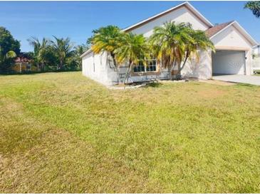 Home exterior featuring a lawn, attached garage, and palm trees at 323 Miami Ln, Kissimmee, FL 34759