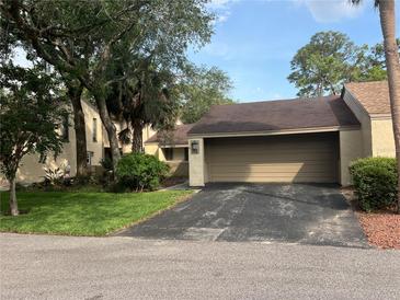 Tan home with an attached garage and a driveway leading up to the house surrounded by many trees at 116 Wild Holly Ln, Longwood, FL 32779