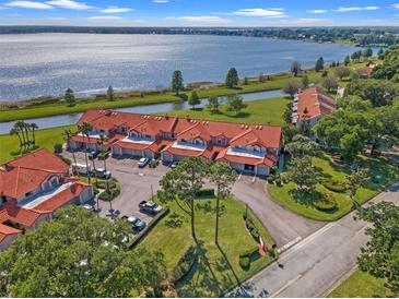 Stunning aerial view of waterfront townhomes with tile roofs, lush landscaping, and private garages near a tranquil lake at 804 Magnolia Pl # 804, Winter Haven, FL 33884