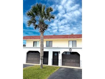Charming two-story home with red roof, attached garages, a palm tree, and a manicured lawn at 64 Ocean Palm S Dr # 64, Flagler Beach, FL 32136