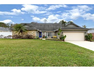 Charming single-story home featuring a stone accent wall, blue door and beautifully landscaped front yard at 13 Twin River Dr, Ormond Beach, FL 32174