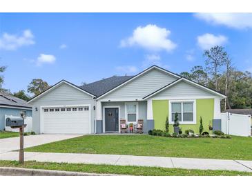 Charming single-story home with gray siding, a green accent wall, well-manicured lawn, and welcoming front porch with rocking chairs at 113 Plumosus Park Dr, Deland, FL 32724