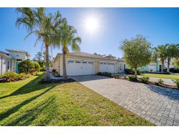 Charming single-Gathering home featuring a two-car garage, paver driveway, lush lawn, and swaying palm trees at 324 Coral Reef Way, Daytona Beach, FL 32124