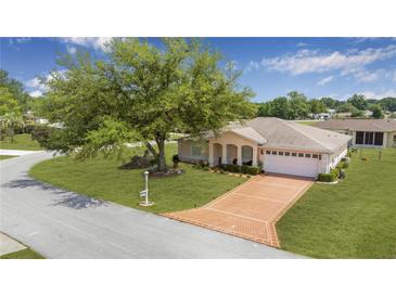 Charming single-story home featuring a brick driveway, manicured lawn, and a large shade tree at 10031 Sw 62Nd Cir, Ocala, FL 34476