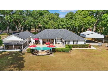 Aerial view of the backyard featuring a pool, patio with red umbrellas, and mature trees on the property at 5865 Ross Creek Rd, Lakeland, FL 33810