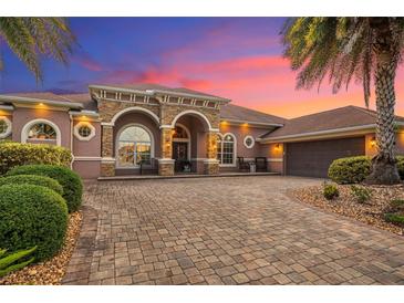 Stunning home with a brick driveway, archway entrance, and lush tropical landscaping and palm trees at sunset at 568 Luna Bella Ln, New Smyrna Beach, FL 32168