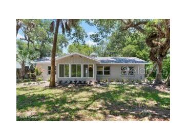 Charming single-story home featuring mature trees, lush green lawn and a cozy enclosed porch at 4901 Sailfish Dr, Ponce Inlet, FL 32127