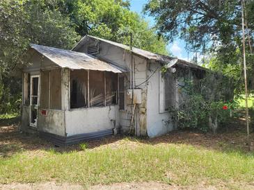 Weathered single story home with peeling paint, screened porch and overgrown landscaping at 110 Montclair Rd, Leesburg, FL 34748