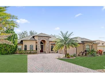 Stunning single-story home showcasing stone accents, a paver driveway, manicured lawn, and lush landscaping at 5418 Meadow Hill Loop, Lady Lake, FL 32159