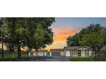 Charming single-story home with a detached garage and metal gate entrance, set against a sunset backdrop at 13832 Bay Lake Rd, Groveland, FL 34736