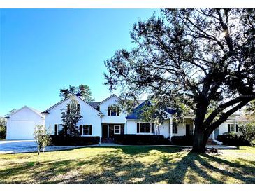 Charming white two-story home with lush lawn and mature shade tree on a sunny day at 26012 Splendid Meadow Ct, Astatula, FL 34705