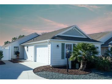 One-story home with attached two-car garage, landscaping, and a palm tree at 1750 Kingfisher Ct, The Villages, FL 32162