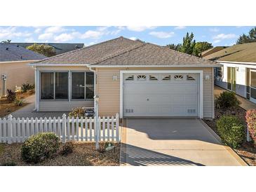 Tan single story house with white picket fence, two-car garage, and sunroom at 1702 Abasco Ct, The Villages, FL 32162