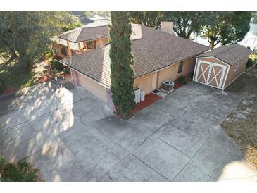 Aerial view of house with large driveway, shed, mature landscaping, and proximity to a lake at 9835 Lakeshore Dr, Clermont, FL 34711