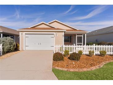 Tan house with white picket fence, two car garage, and screened porch at 1387 Zest Ave, The Villages, FL 32163