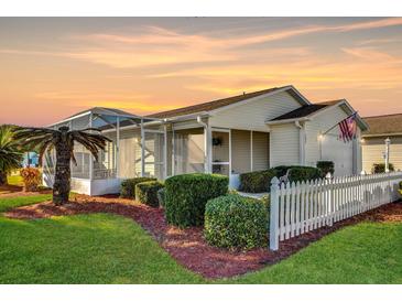 Charming single-story home featuring a manicured lawn, white picket fence, and an enclosed patio, all bathed in the warm glow of sunset at 202 Estrada Pl, The Villages, FL 32159