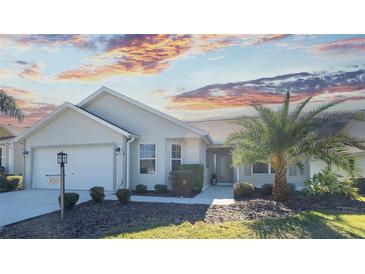 Tan one-story house with attached garage, landscaping, and palm trees at 670 Murphys Estate Dr, The Villages, FL 32162