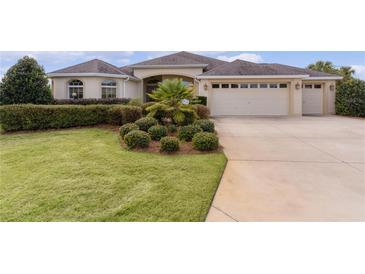 Tan one-story house with landscaped yard, three-car garage, and lush green lawn at 3538 Mistletoe Ct, The Villages, FL 32163