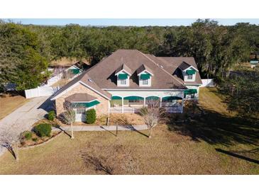 Charming home boasts a covered porch, manicured lawn, stone accents, and mature trees at 37008 Shalimar Dr, Fruitland Park, FL 34731