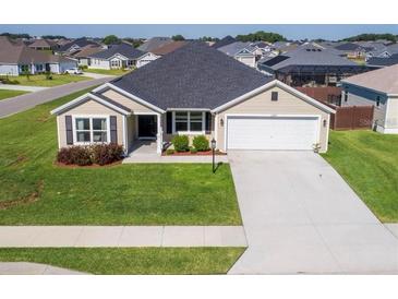 Tan house with gray roof, two-car garage, and well-manicured lawn at 11272 Stewart Loop, Oxford, FL 34484