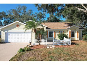 Cute yellow house with white picket fence, landscaping, and a two-car garage at 25107 Meriweather Rd, Leesburg, FL 34748