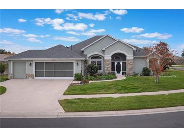 Landscaped one-story house with light green exterior, two-car garage and screened porch at 27504 Stoney Brook Dr, Leesburg, FL 34748