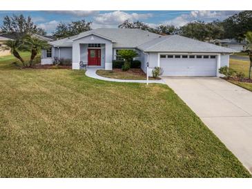 Single-story home with gray siding, red door, and two-car garage, nicely landscaped yard at 27302 Orchid Glade St, Leesburg, FL 34748