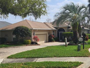 Charming single-story home features a manicured lawn, lush landscaping, and a brick driveway leading to an attached garage at 6216 Landings Blvd, Lady Lake, FL 32159