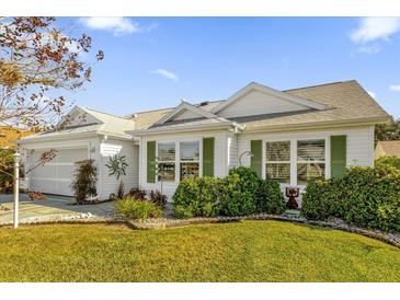 White house with green shutters, landscaped lawn, and a two-car garage at 16967 Se 93Rd Cuthbert Cir, The Villages, FL 32162