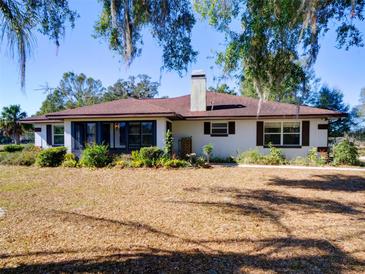 White house with brown roof, large yard, and mature trees at 1199 Cr 542G, Bushnell, FL 33513