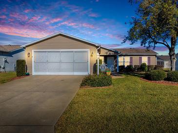 Tan house with a two-car garage and landscaped lawn at 2009 Claudio Ln, The Villages, FL 32159