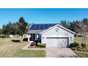 Gray house with solar panels, brick driveway, and landscaped yard at 409 Silver Maple Rd, Groveland, FL 34736