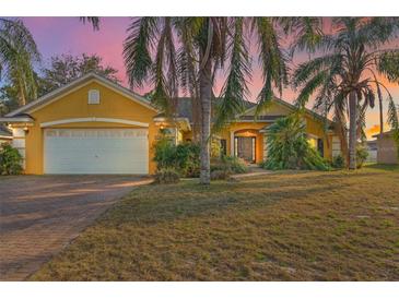 Charming yellow home with a two-car garage, brick driveway, and mature palm trees at 35808 Rose Moss Ave, Leesburg, FL 34788