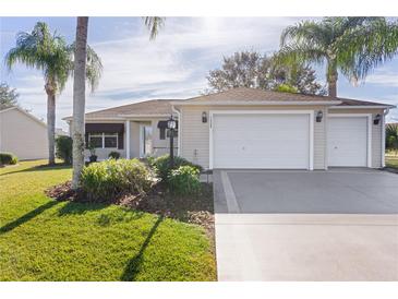 Beige house with two-car garage, landscaped lawn, and palm trees at 1509 Lakewood Dr, The Villages, FL 32162