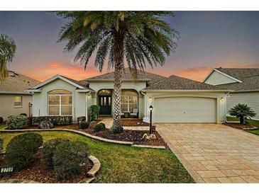 Charming single-story home with a large palm tree, manicured lawn, and paver driveway at 2709 Astoria Ave, The Villages, FL 32162