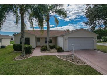 Charming single-story home with a well-manicured lawn, palm trees, and attached garage at 8338 Se 178Th Deveaux Ln, The Villages, FL 32162