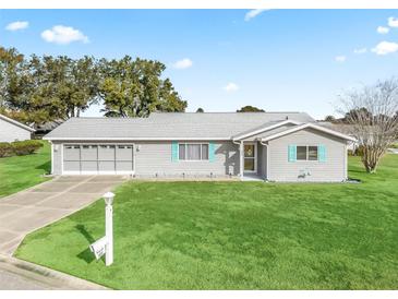 Gray house with teal accents, two-car garage, and spacious lawn at 9897 Se 178Th Pl, Summerfield, FL 34491