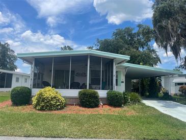 White single-wide home with carport, screened porch, and landscaped yard at 185 Jacaranda Dr, Leesburg, FL 34748