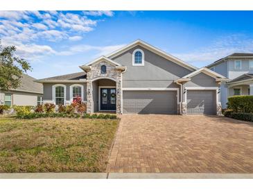 Two-story house with gray siding, three-car garage, and a brick driveway at 2064 Lula Rd, Minneola, FL 34715