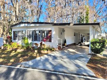 White single-wide mobile home with carport, landscaping, and golf cart at 105 Royal Palm Dr, Leesburg, FL 34748