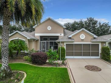 Tan house with a screened porch, two-car garage, and landscaped yard at 4985 Rainbow Trout Rd, Tavares, FL 32778