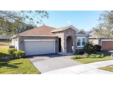 Charming single-story home with stone accents, brick driveway, manicured lawn, and attached two-car garage at 96 Silver Maple Rd, Groveland, FL 34736