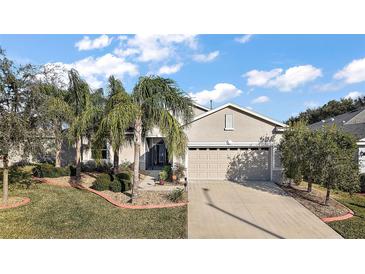 Tan house with palm trees, two-car garage, and landscaped yard at 27008 Camerons Run, Leesburg, FL 34748